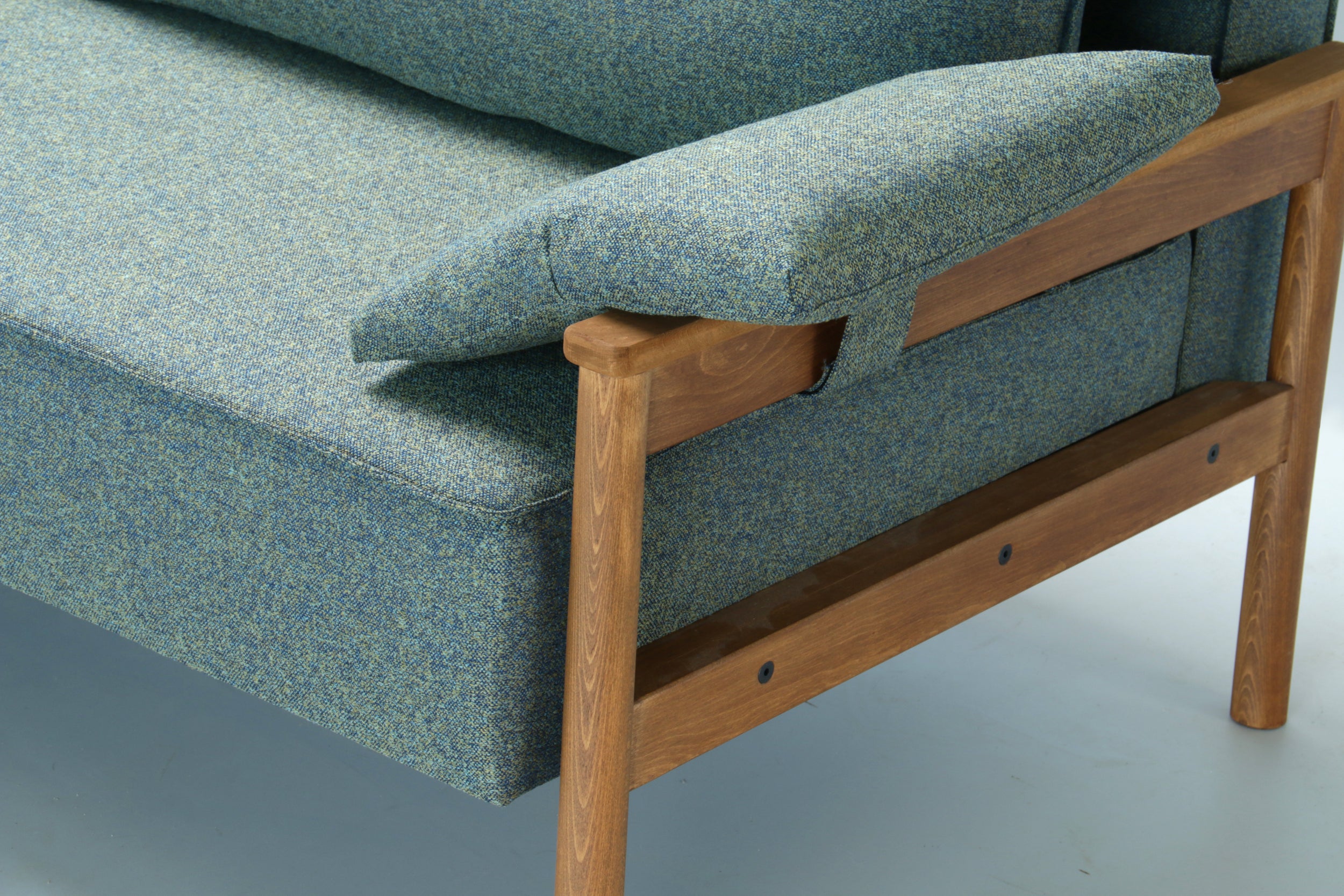Detail view of green Alpine sofa bed with wooden armrest on a white background.