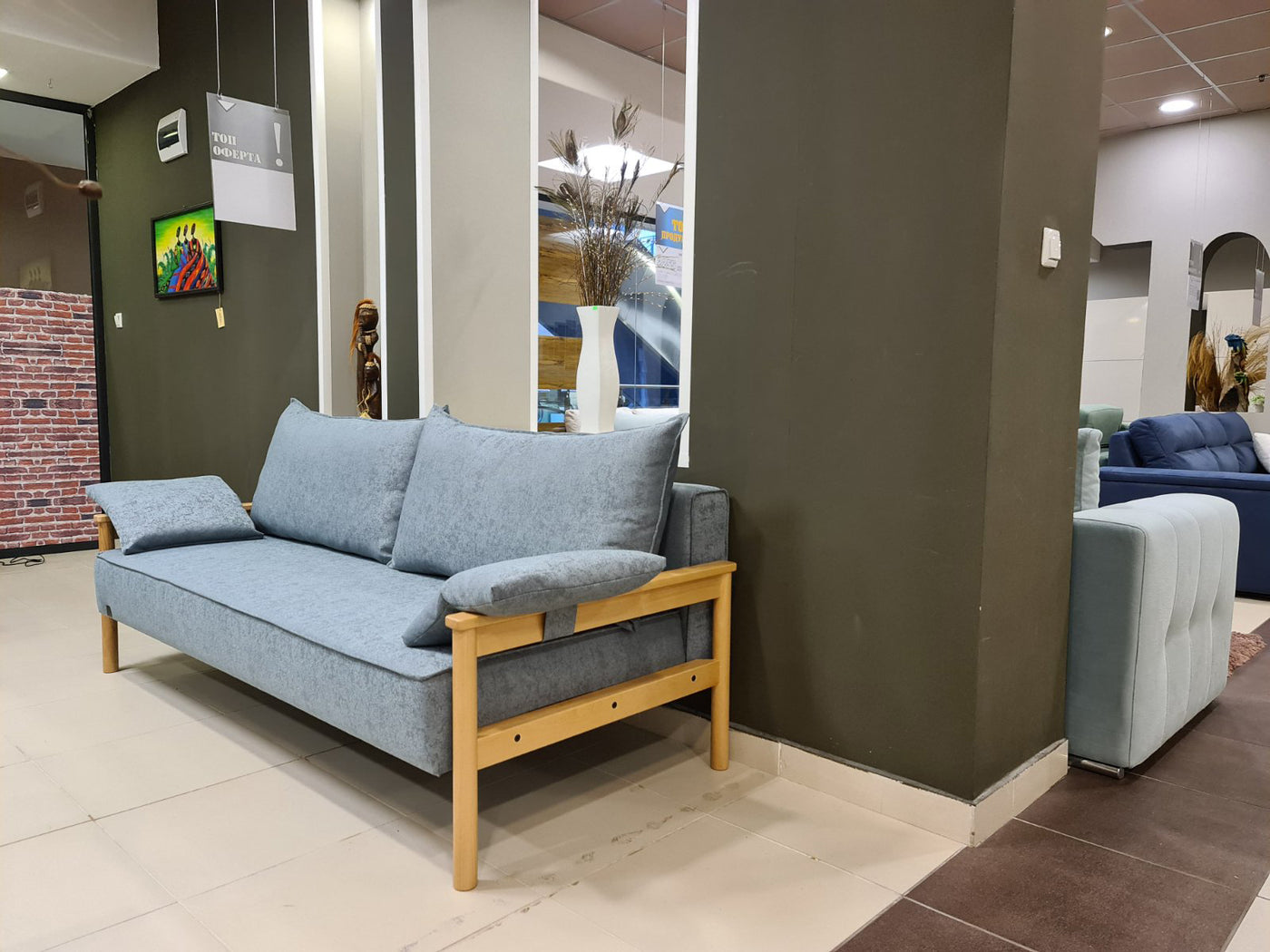 Blue Alpine sofa bed with wooden frame in a showroom setting.