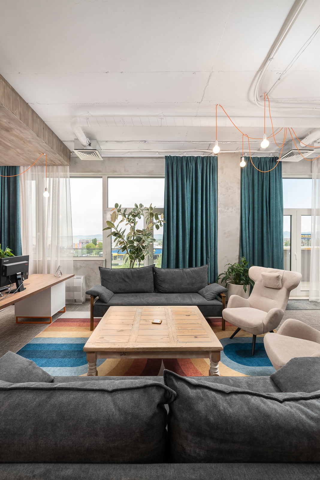 Modern living room with gray Alpine sofa bed and  a wooden coffee table, and large windows with blue curtains.