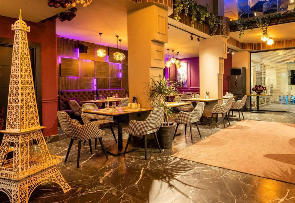Restaurant interior with Eiffel Tower model, tables, and many Andre chairs.