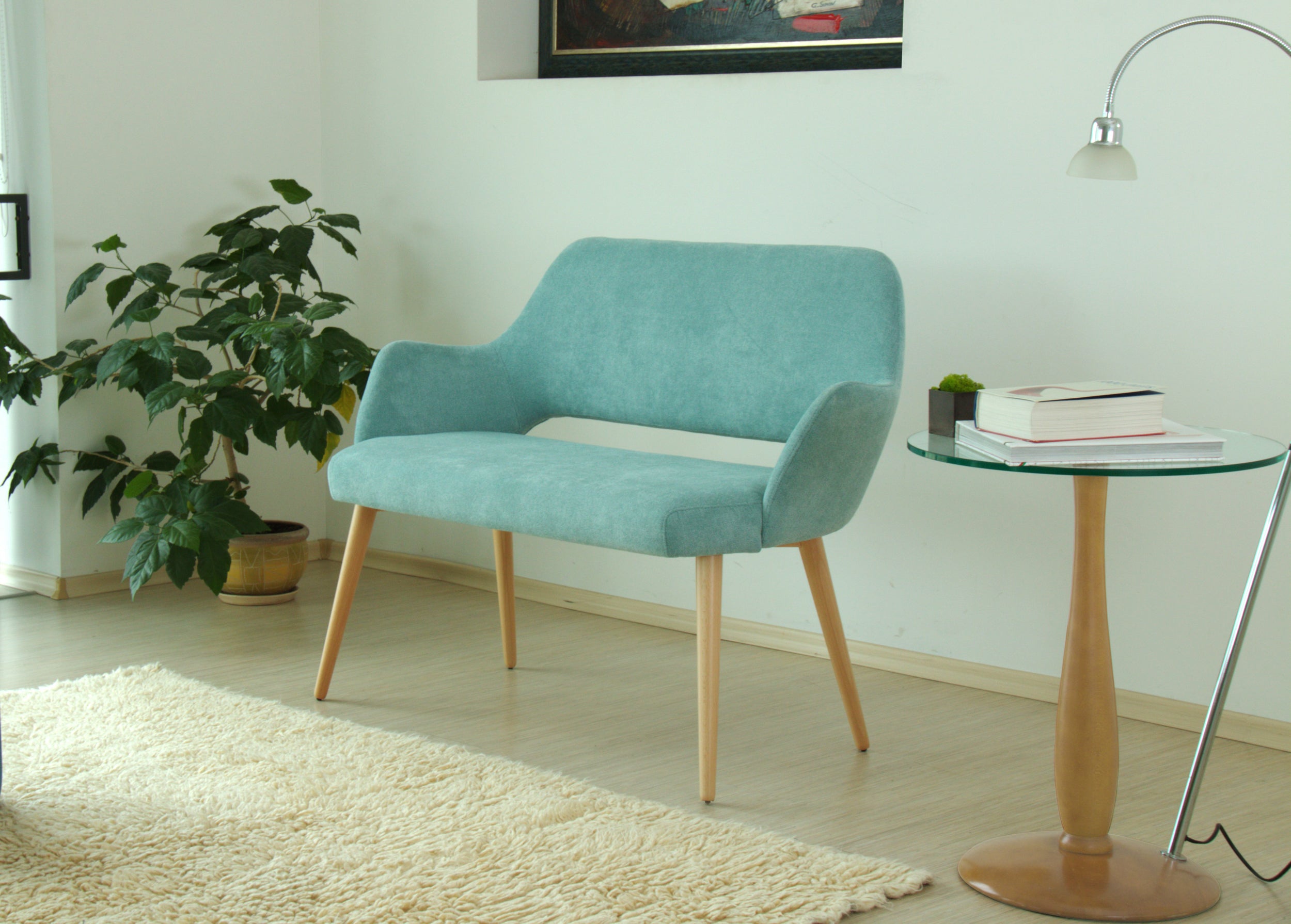 Teal sofa Andre in a modern living room with a side table and plant.