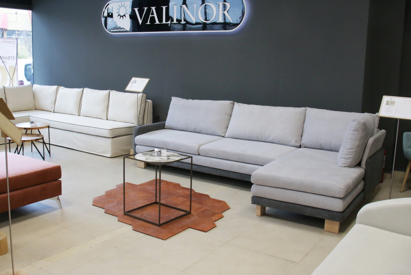 Gray sectional sofa B12 in a showroom with 'Valinor' branding on the wall.
