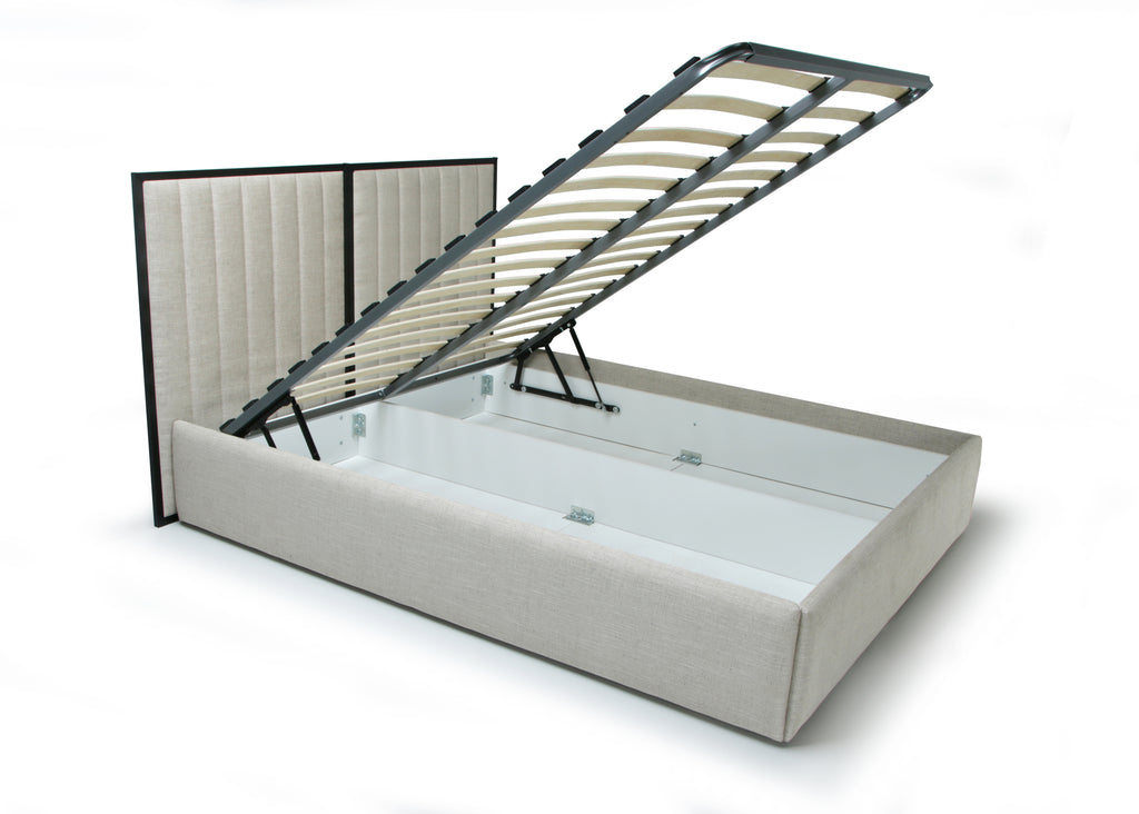 An upholstered storage bed with a lift-up slatted frame, shown open to reveal the spacious bed frame and white storage compartment underneath. The headboard is vertically slatted with a tufted panel design, and the entire bed frame is upholstered in a light beige fabric.