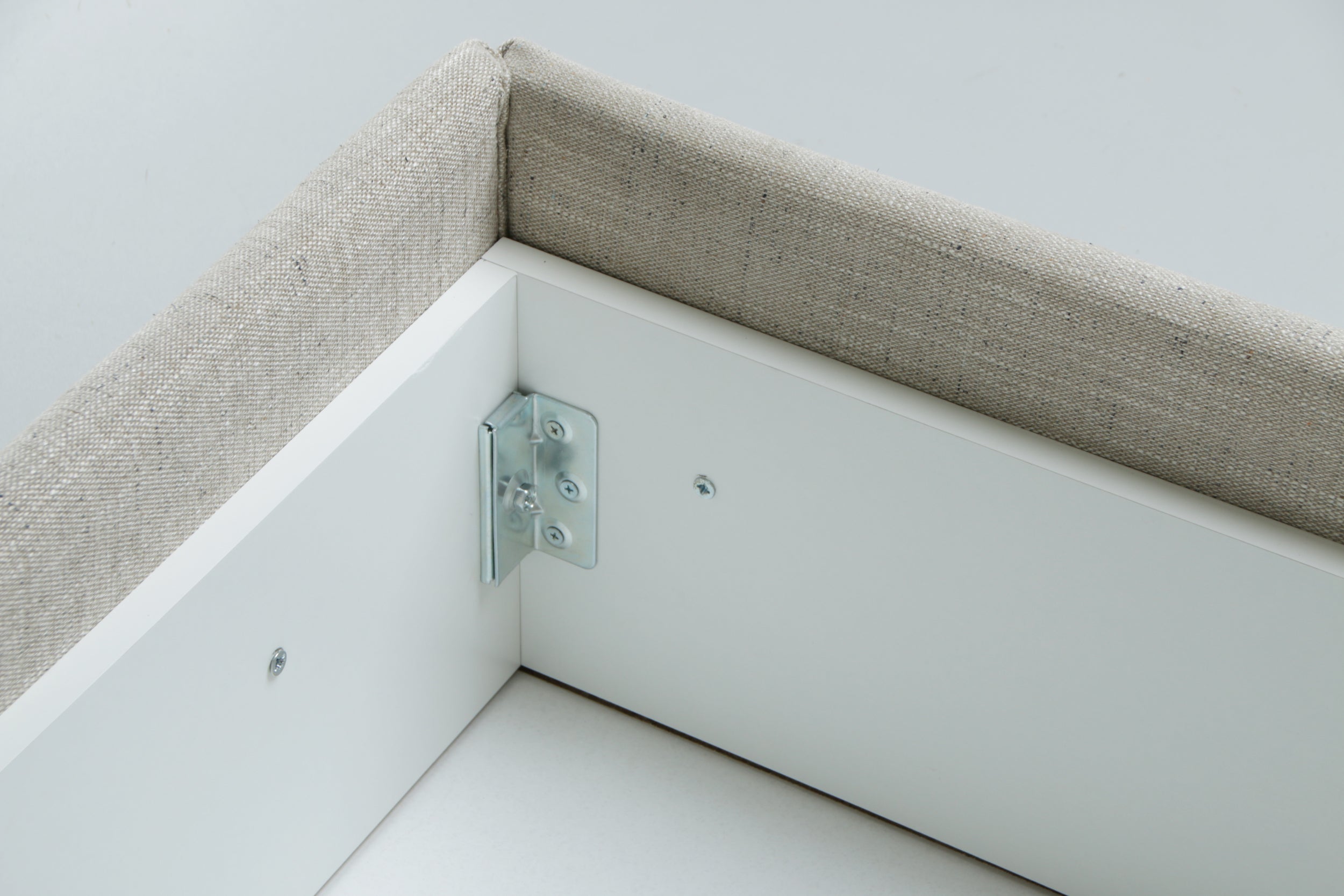 Metal bracket on a white and beige corner of a bed chest.