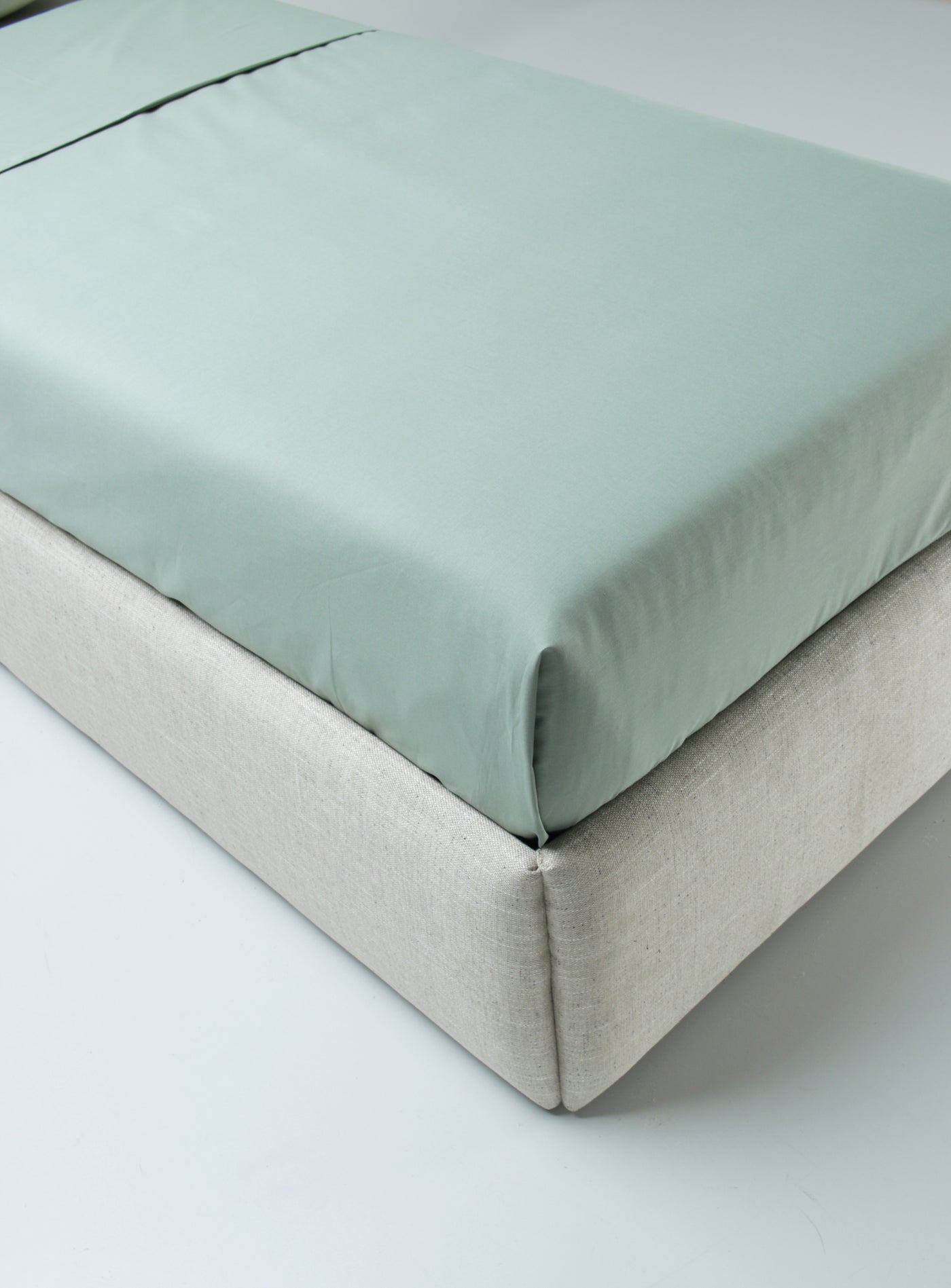 Green fitted sheet on a bed with a white background