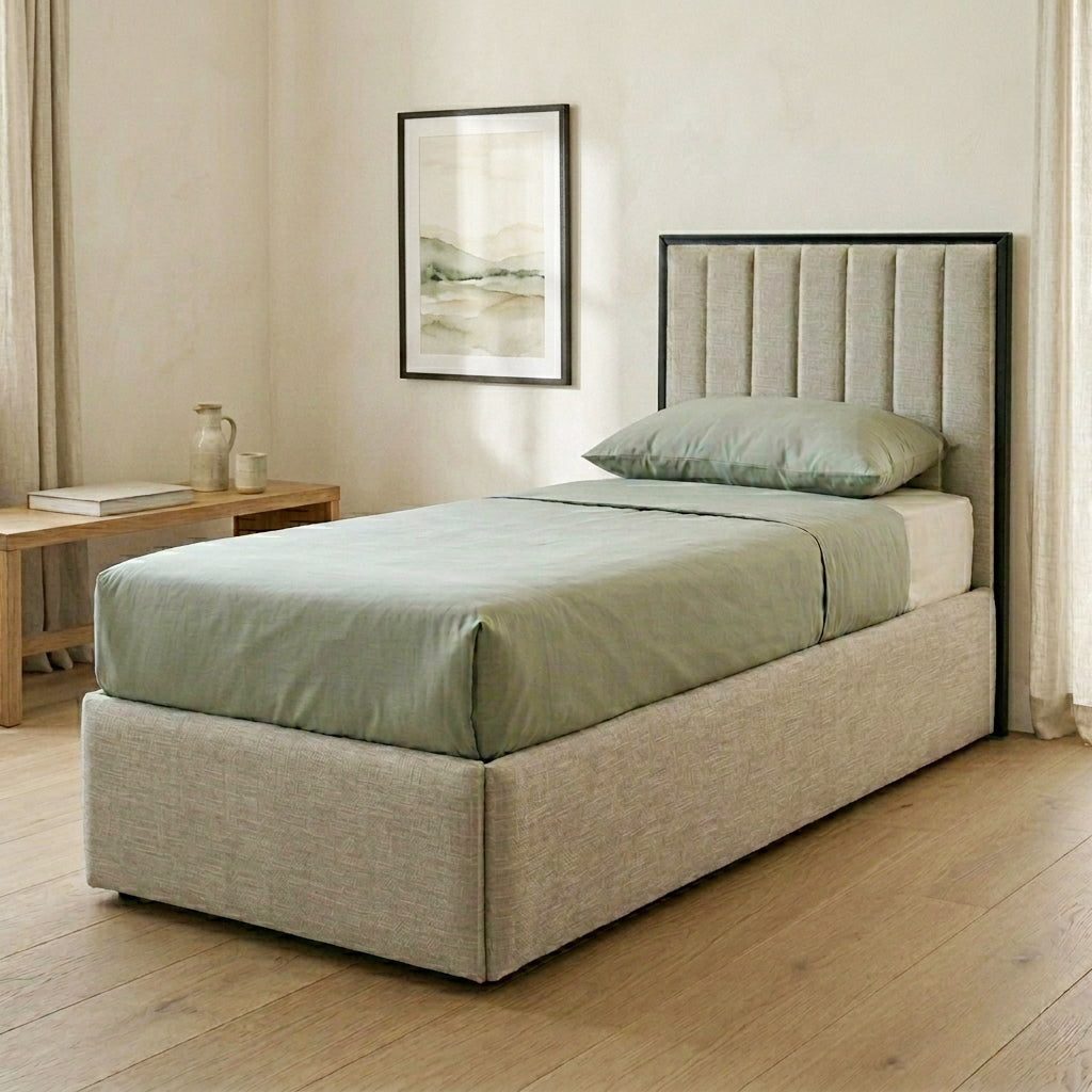Beige upholstered bed with green bedding in a room with a framed picture on the wall and upholstered  headboard.