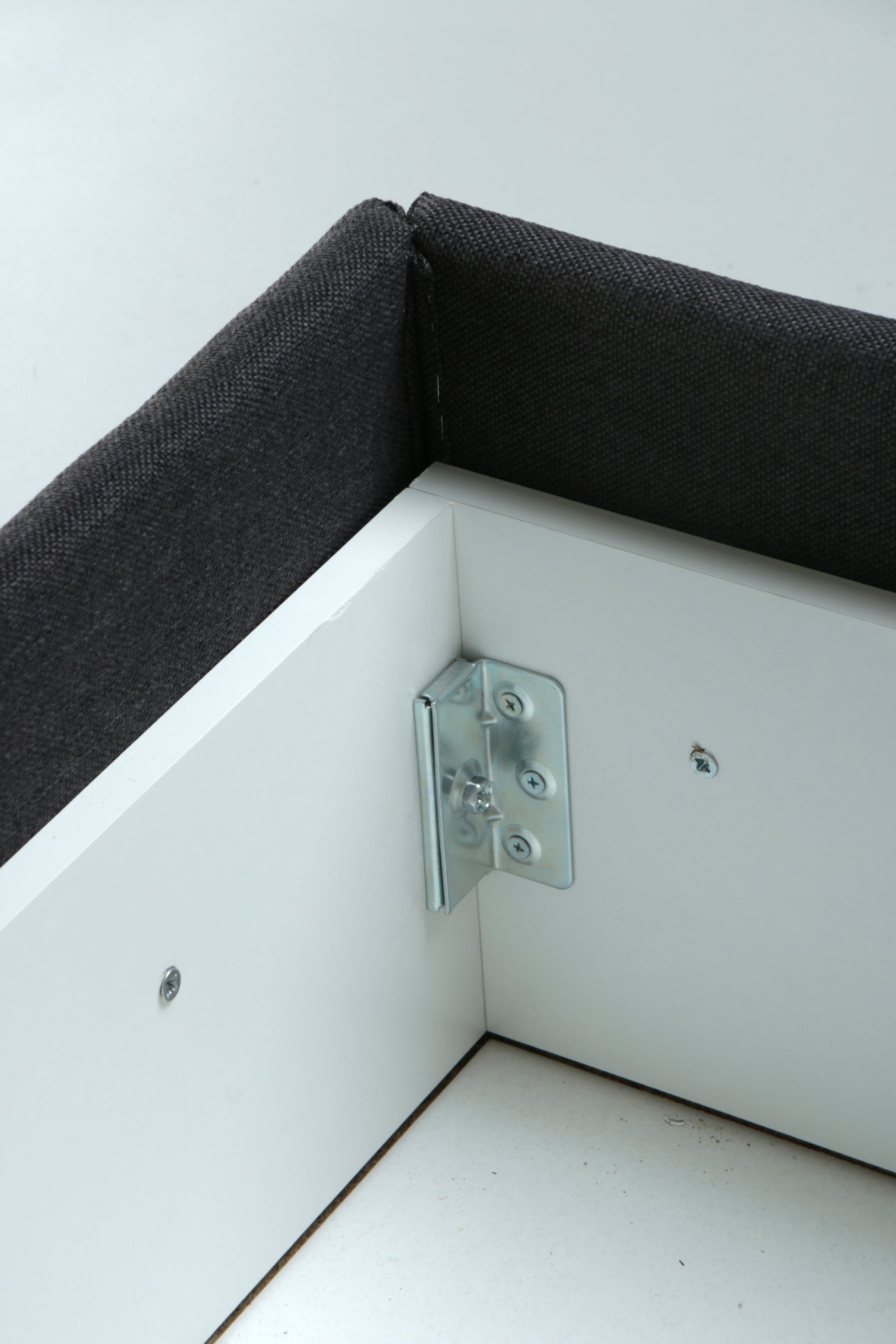 Close-up of a white storage box corner with dark charcoal gray fabric lining and a silver metal corner bracket.