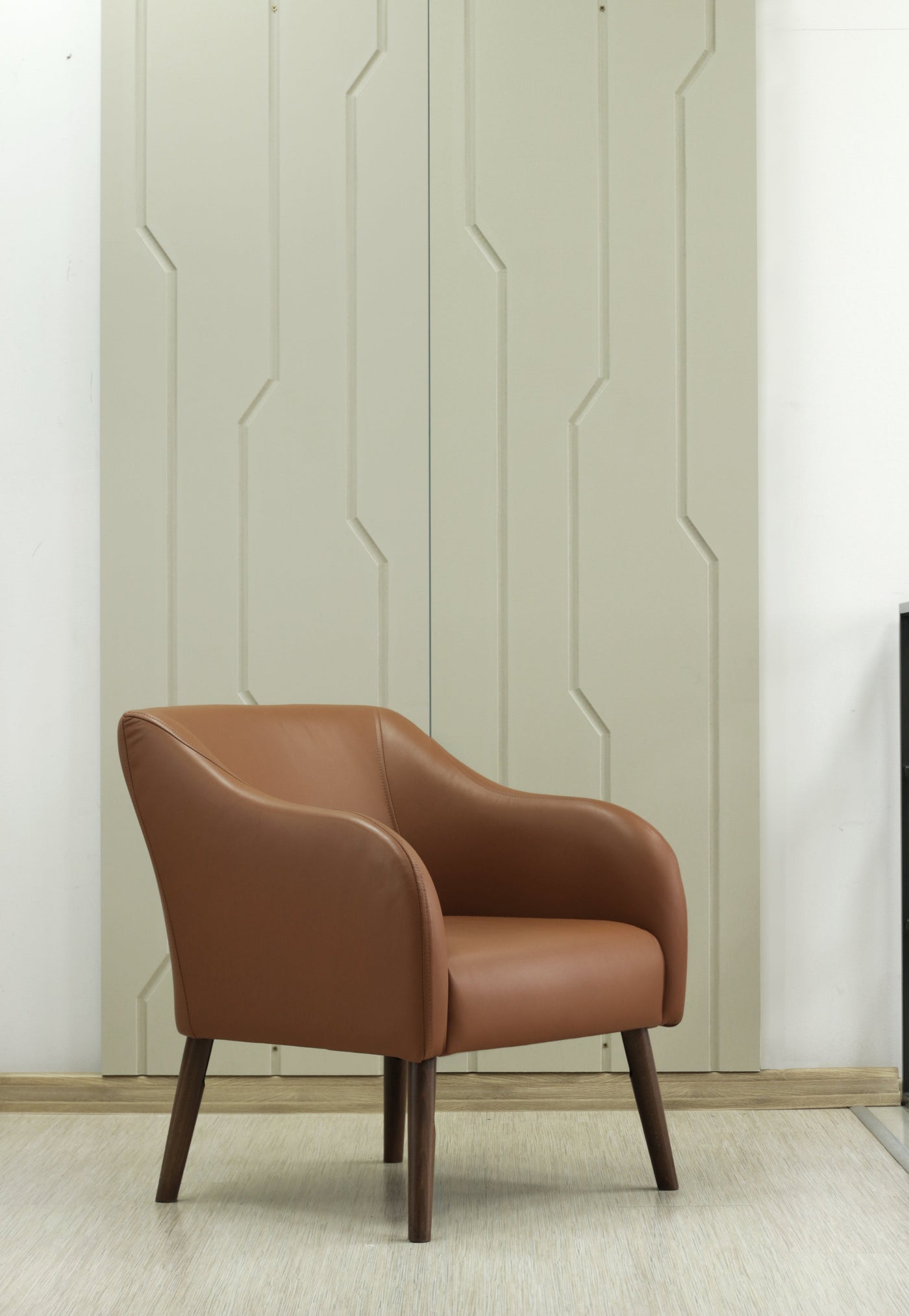 Brown leather Juno armchair against a decorative  milled MDF wall with geometric pattern in artmodern style.