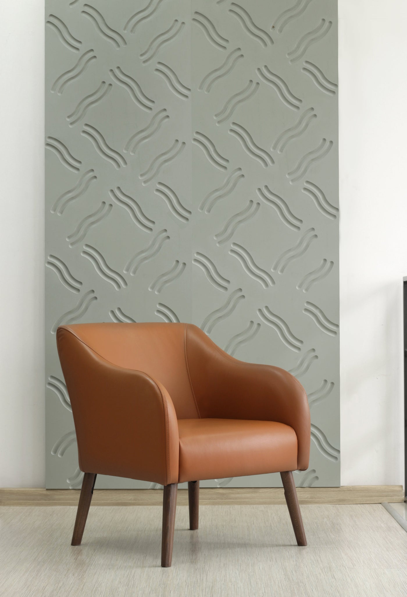 Brown leather Juno armchair against a decorative  milled MDF wall with geometric wave pattern.