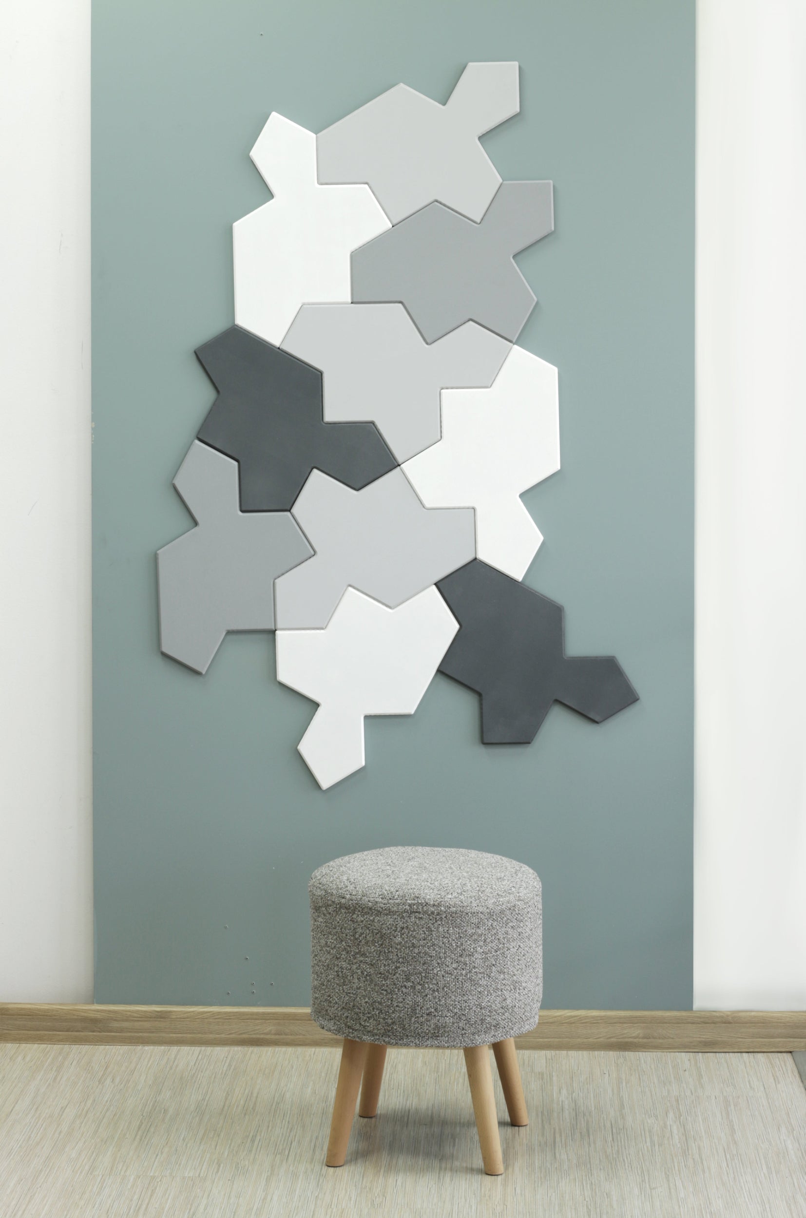 Geometric wall art of Chiral aperiodic monotile panels on a gray wall with a small stool in front.