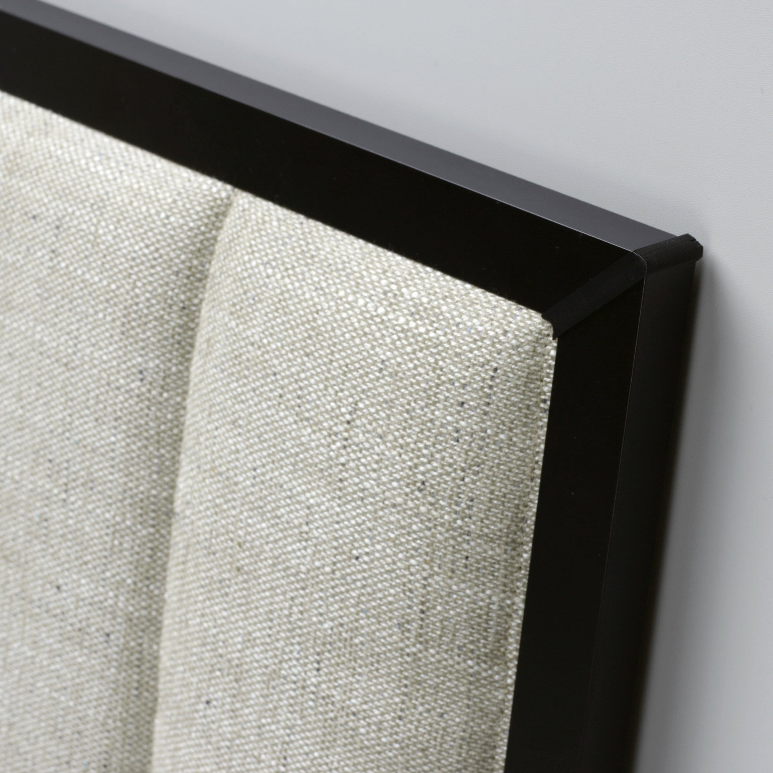 Close-up of a  headboard with a stitched beige upholstery and black frame on a light gray background.