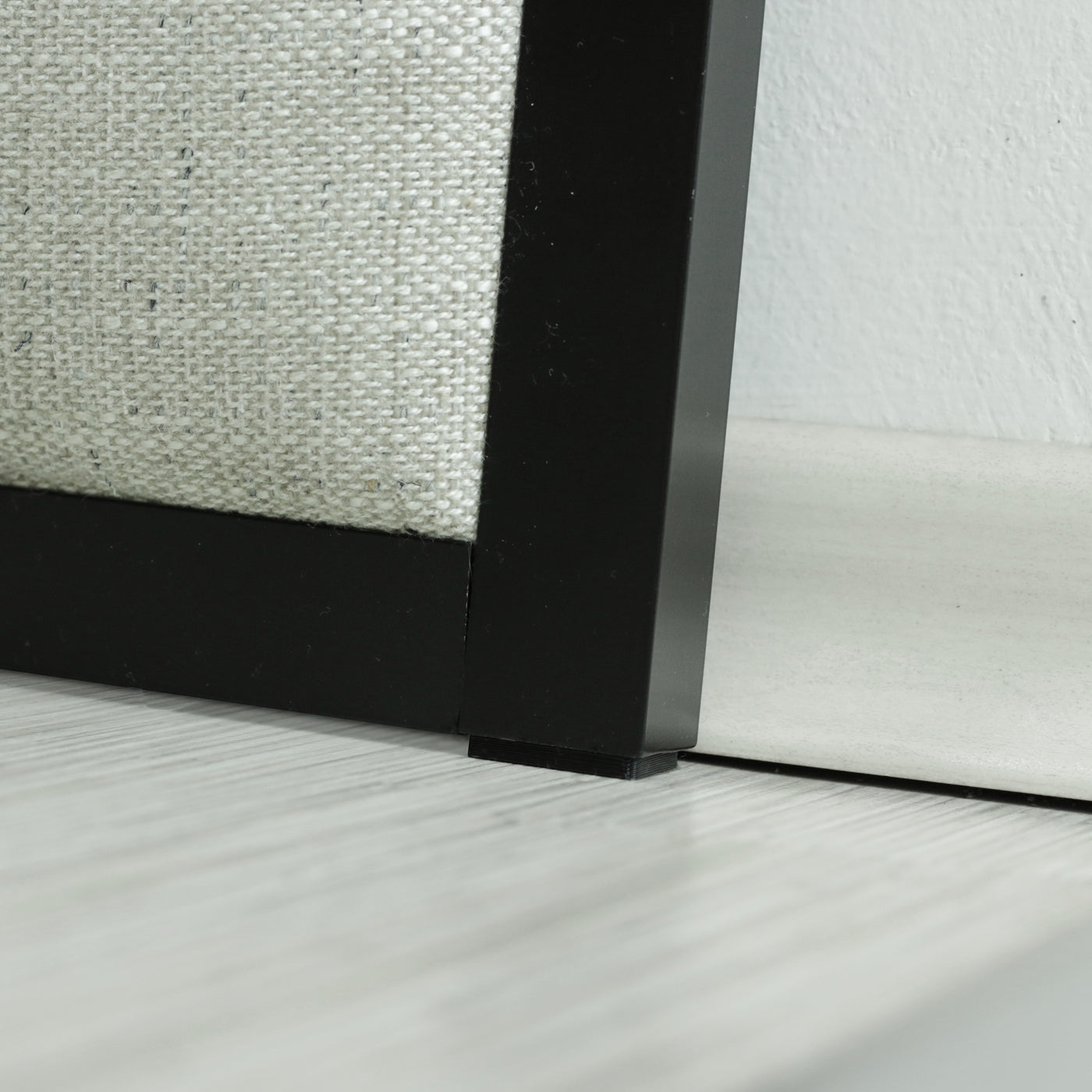 Close up of headboard with a beige upholstery and black frame.