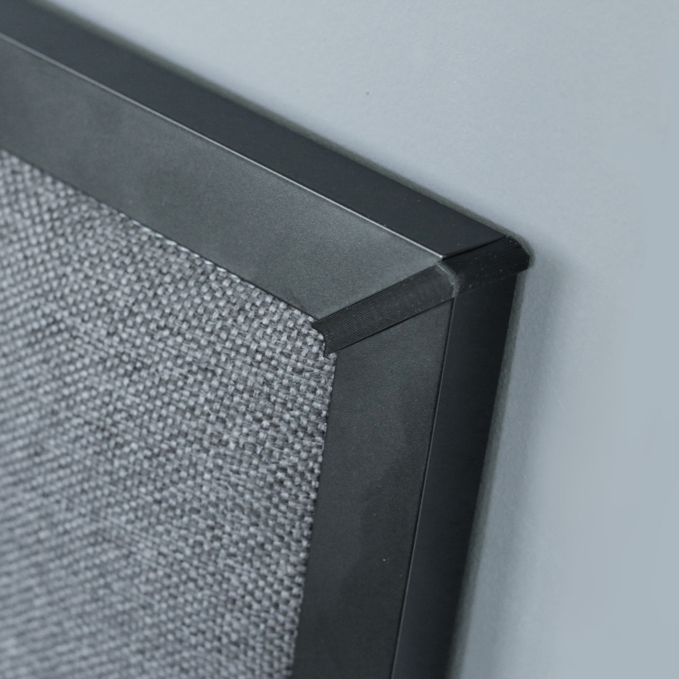 Close-up of a  headboard with a dark grey upholstery and black frame on a light gray background.