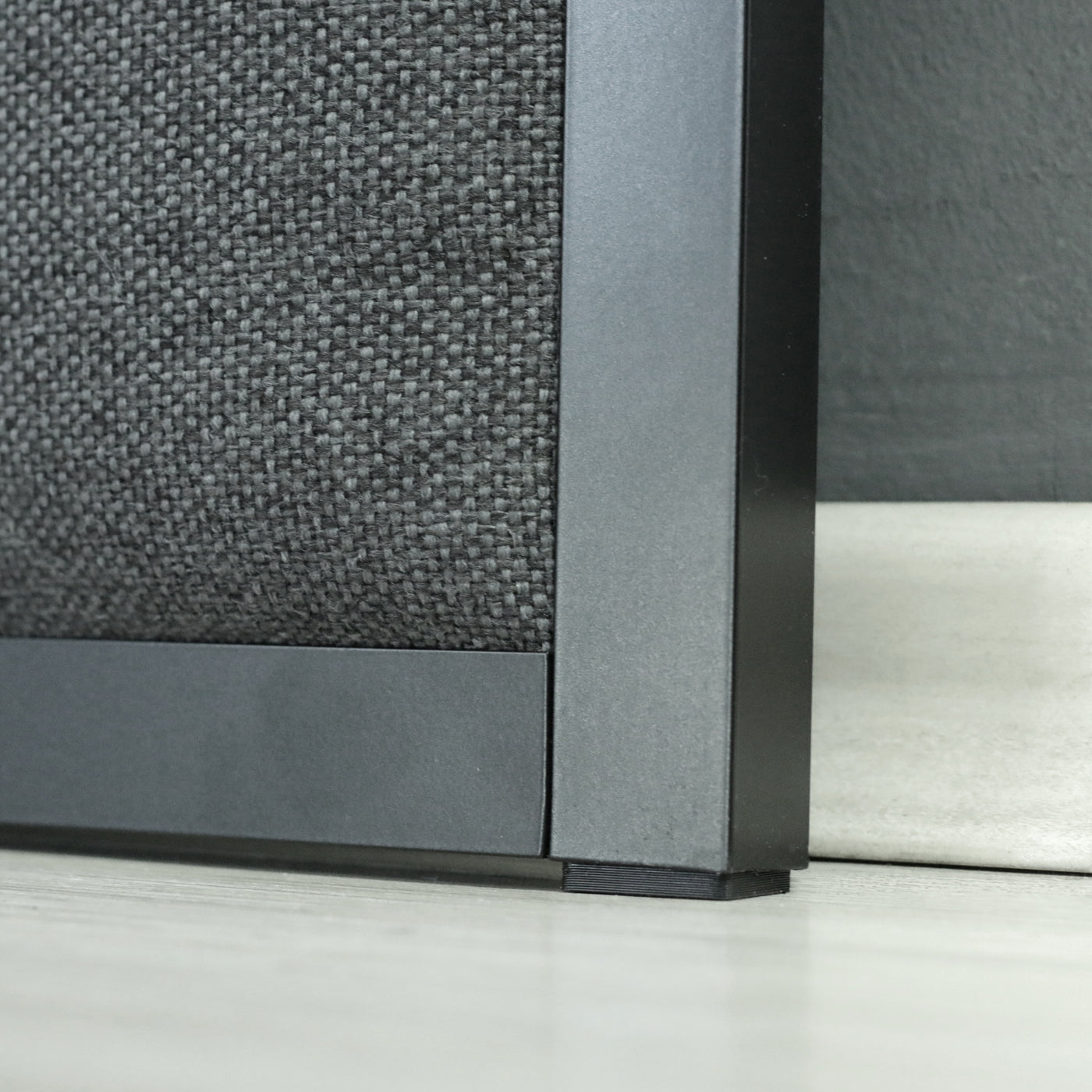 Close up of headboard with a dark grey upholstery and black frame.