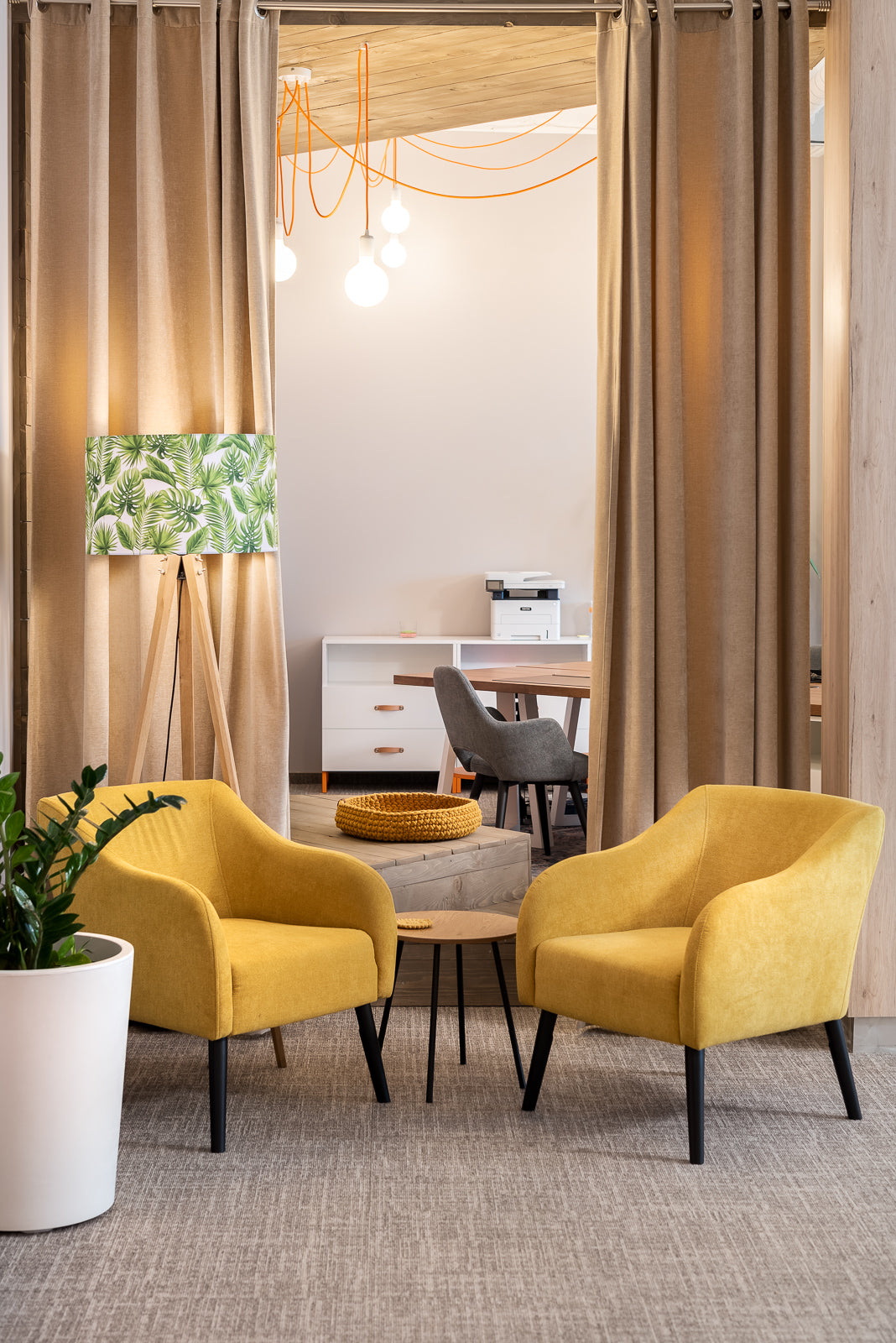 Two yellow Juno armchairs in a modern office setting with a desk and lamp in the background.