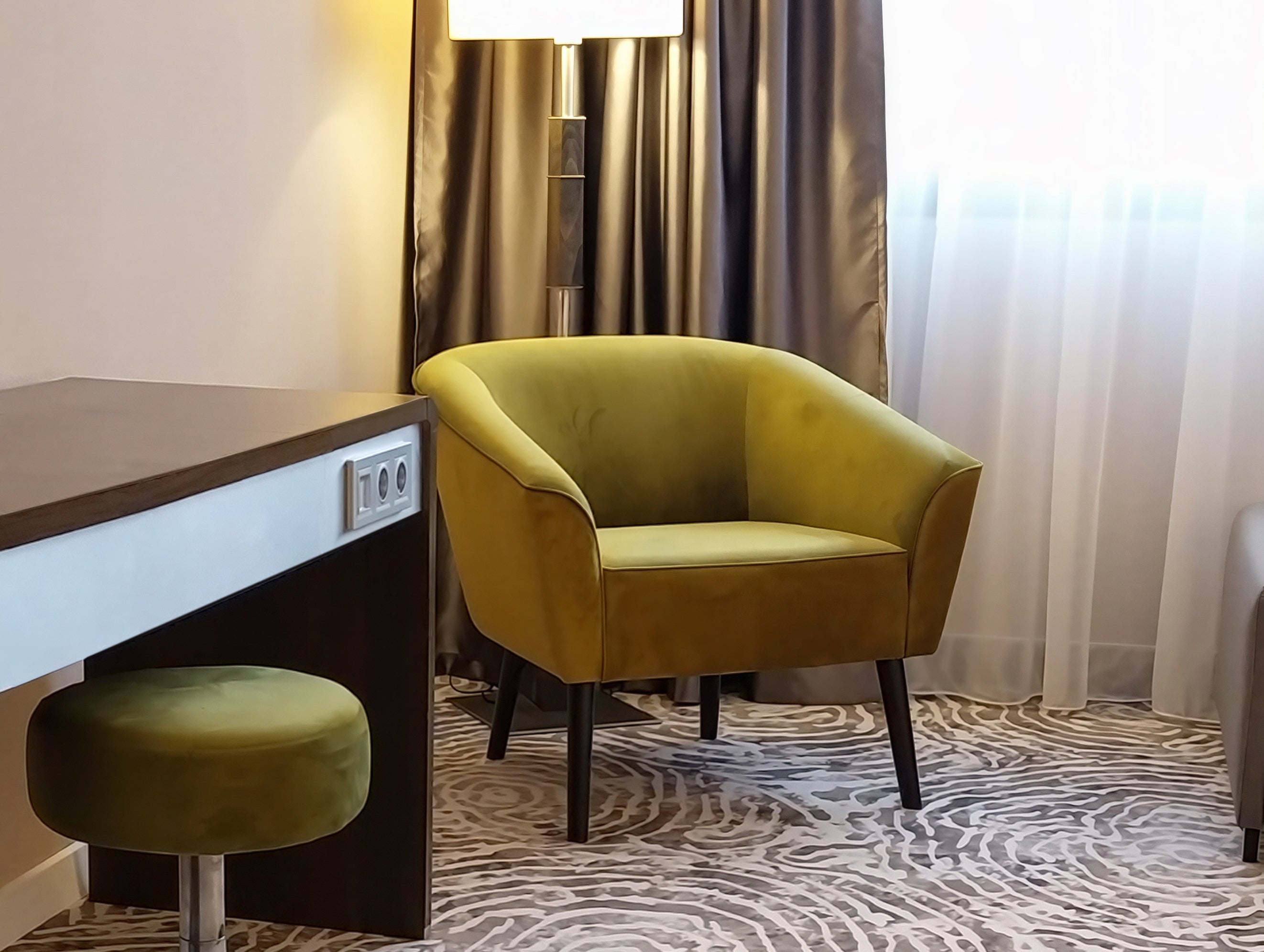 Green armchair Leonardo with wooden legs in hotel room with curtains and desk