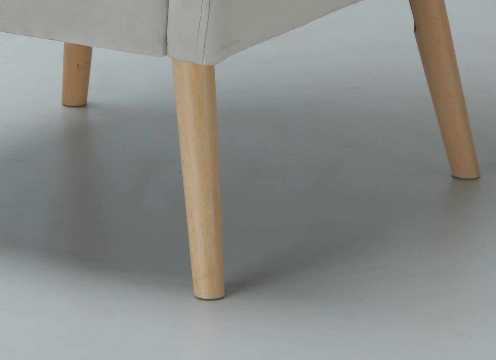 Close-up of a Lola armchair with beige cushioned seat and light wood legs on a plain background