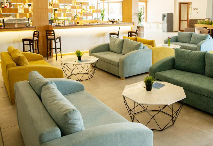 Modern hotel lobby with green and yellow MAX sofas, coffee tables, and decorative plants.