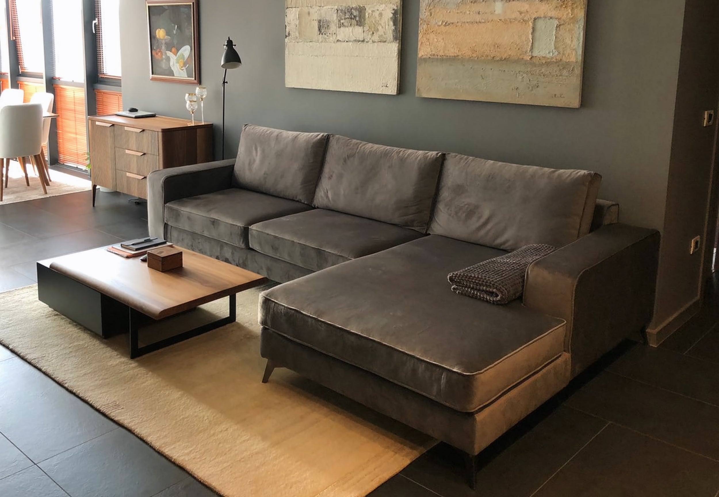 A modern gray fabric sectional Connor sofa with a chaise lounge, styled in a contemporary living room with a wooden coffee table, beige rug, and abstract wall art.